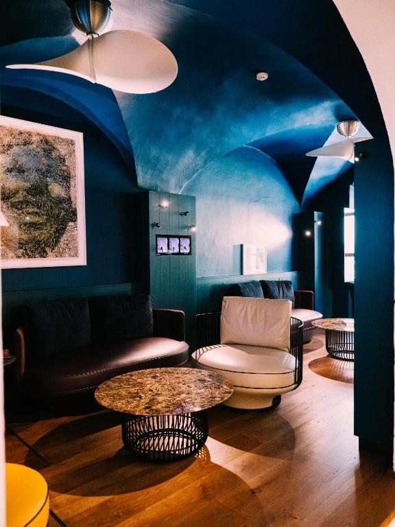 Unique Boutique Hotels in Salzburg 37 A modern lounge inspired by Boutique Hotels in Salzburg, featuring a blue arched ceiling, dark sofa, white armchairs, round marble coffee tables with metal bases, wooden floor, and wall art under soft ambient lighting.