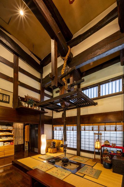 Looking for the Best Ryokan in Takayama? 13 Traditional Japanese room with exposed wooden beams, tatami mats, low tables, an irori hearth, and shoji screens—evoking the cozy, rustic atmosphere of the Best Ryokan in Takayama. Shelves hold neatly folded fabrics on one side.