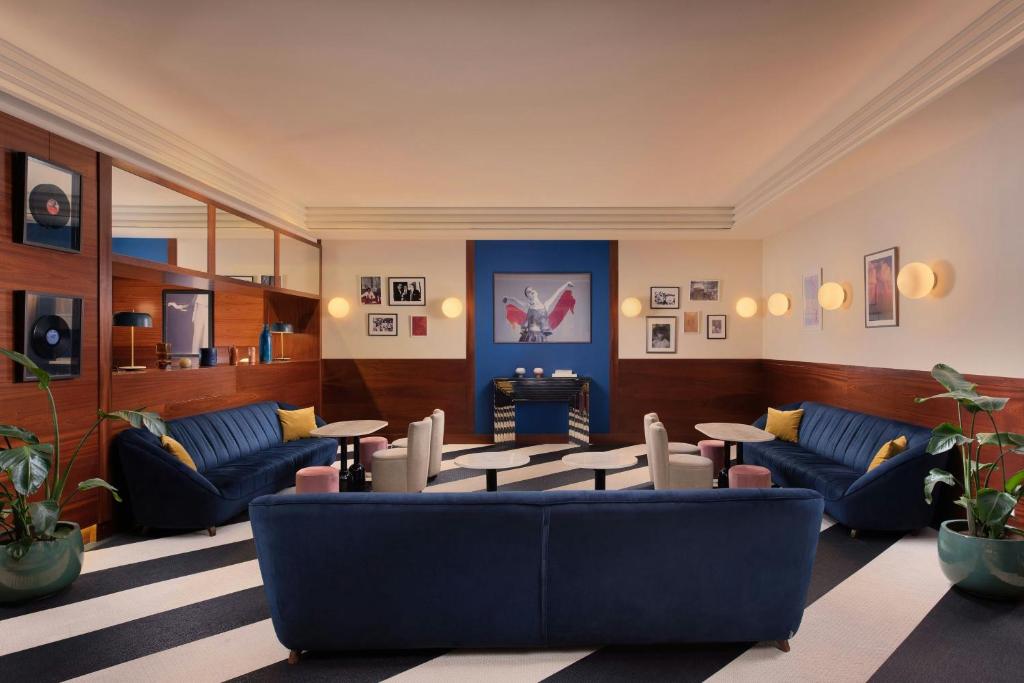 8 Unique Boutique Hotels in Bilbao Spain 17 A stylish lounge in the spirit of boutique hotels in Bilbao, with blue velvet sofas, round tables, and striped carpeting. Green plants and wood paneling add a cozy, modern touch alongside framed art and vinyl records on the walls.