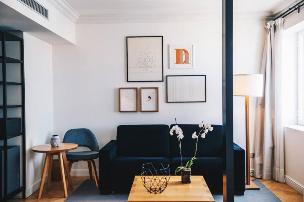 Where to Stay in Madrid: 14 Best Hotels 38 A modern living room—ideal inspiration for those wondering where to stay in Madrid first time—with a dark sofa, wooden coffee table, wire basket and orchids, soft lighting, a vase on the side table, framed artwork, and sunlight streaming through the window.