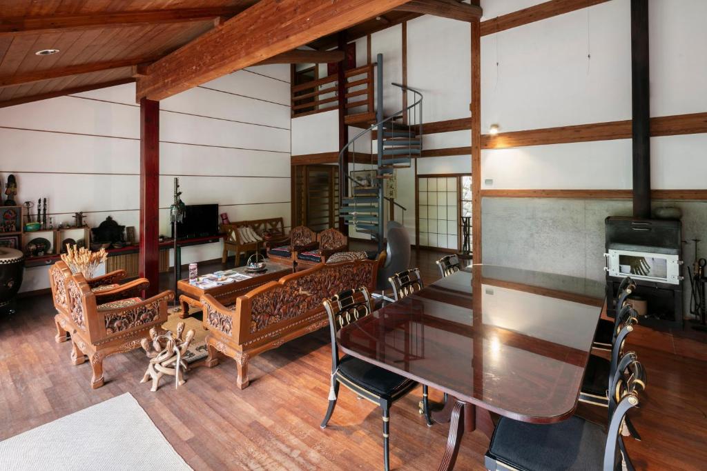 8 BEST Ryokans in Osaka 25 A spacious living and dining area features wooden floors, ornate carved furniture, a dark dining table with black chairs, a spiral staircase, and a wood stove—echoing the elegant style found in ryokans in Osaka.