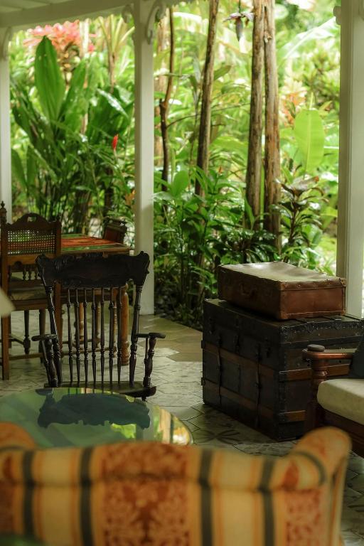 Unique Hotels in Costa Rica: Top Stays 11 A veranda at one of the unique hotels in Costa Rica features vintage wooden chairs, stacked antique trunks, a glass-top table, and a cushioned sofa, all surrounded by lush green tropical plants and trees.