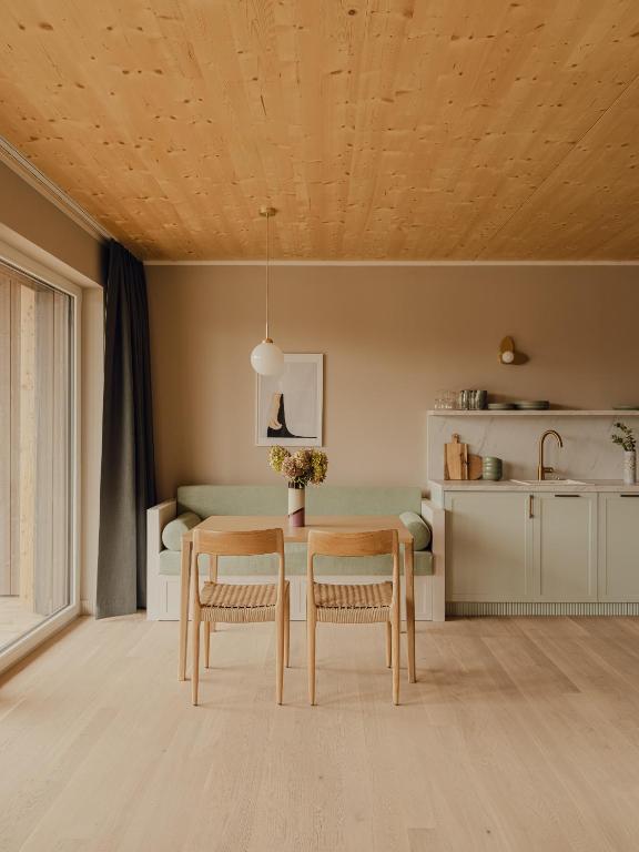 Unique Boutique Hotels in Salzburg 4 Minimalist kitchen and dining area with light wood floors and ceiling, a small green sofa, two wooden chairs at a table with a vase of flowers—reminiscent of the chic interiors found in boutique hotels in Salzburg.