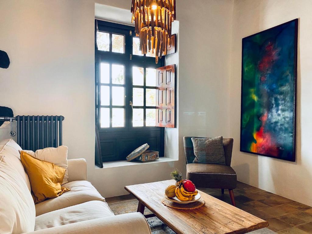 Unique Adults Only Hotels in Lanzarote 22 A cozy living room with a white sofa, yellow pillow, wooden coffee table with fruit, gray armchair, large colorful abstract painting, and a window letting in natural light beneath a wooden chandelier—like those found in Adults Only Hotels in Lanzarote.