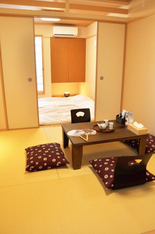 8 BEST Ryokans in Osaka 10 A traditional Japanese tatami room, inspired by ryokans in Osaka, features a low wooden table, floor cushions, tea set, and sliding shoji doors. In the next room, a futon bed rests near a window filled with natural light.