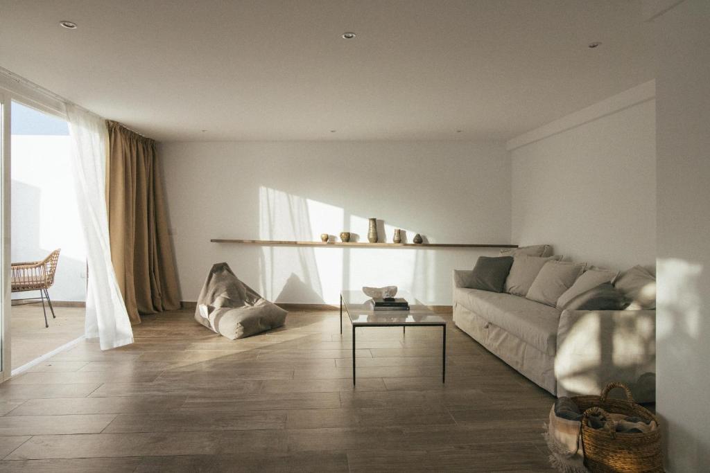 Unique Adults Only Hotels in Lanzarote 18 Minimalist living room with a beige sofa, low table, bean bag, and decorative vases on a wall shelf—reminding you of the serene style found in Adults Only Hotels in Lanzarote. Sunlight streams through large sliding doors with tan curtains and wooden floors.