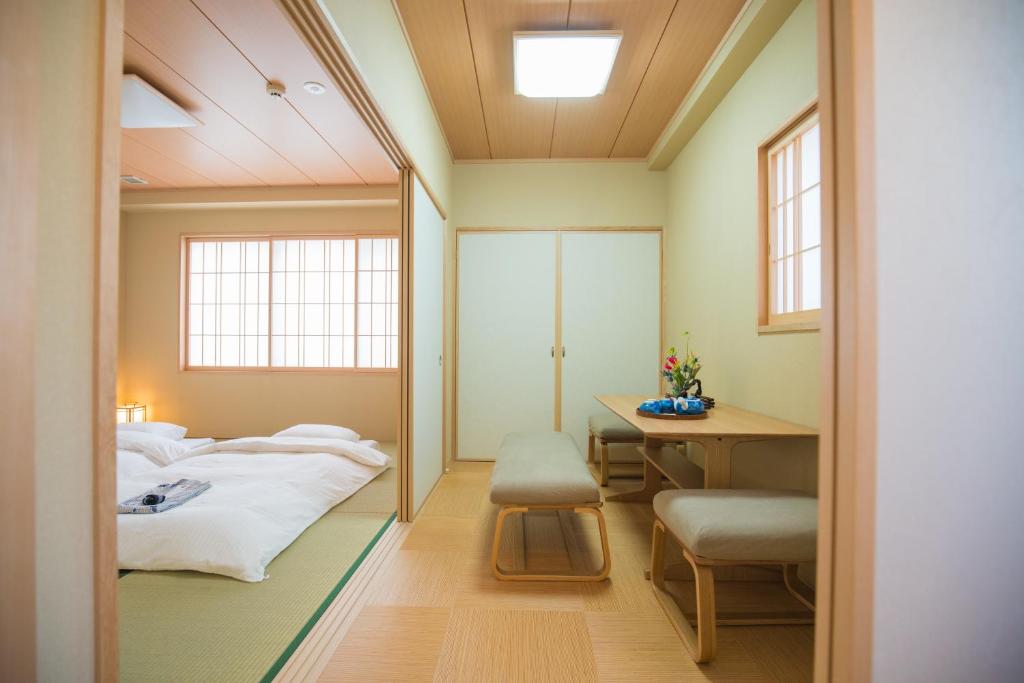 8 BEST Ryokans in Osaka 13 A minimalist Japanese-style room inspired by ryokans in Osaka, with tatami mats, futons on the floor, sliding shoji doors, a small wooden table with benches, and a window letting in soft natural light.