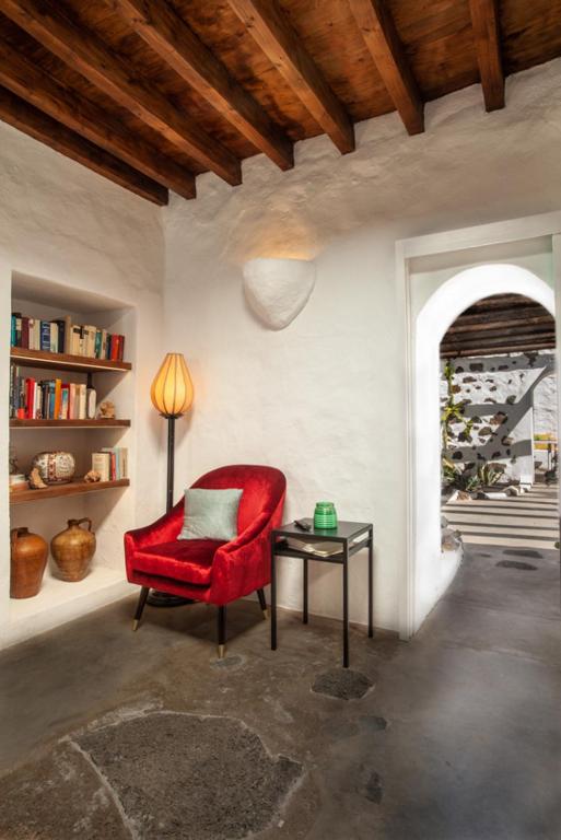 Unique Adults Only Hotels in Lanzarote 17 A cozy reading nook with a red velvet armchair, a side table, and a lamp sits beside a built-in bookshelf and ceramic vases—reminiscent of the intimate spaces found in Adults Only Hotels in Lanzarote. Sunlight streams through an arched doorway to stone-accented outdoors.