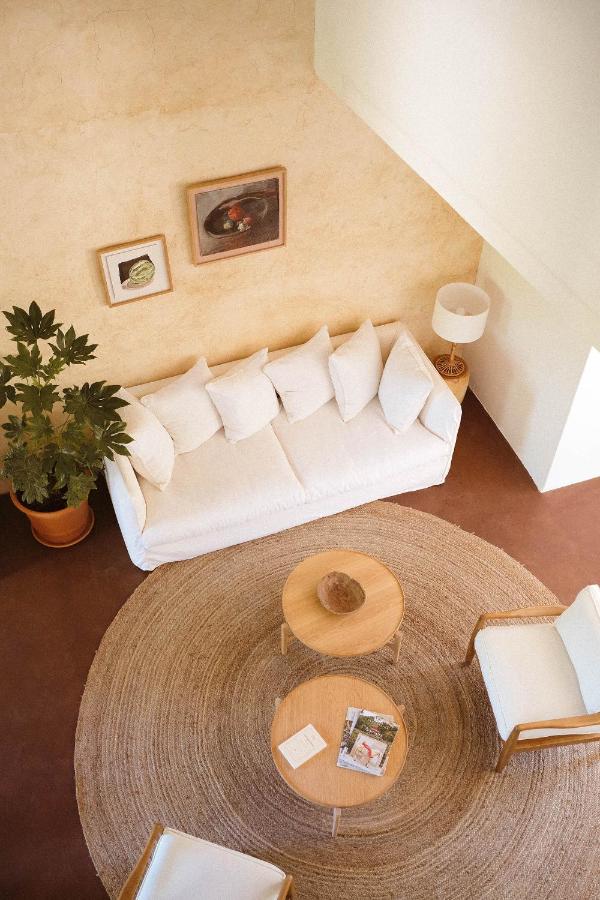 11 Unique Places to Stay in Provence 8 A cozy living room with a white sofa, plush pillows, and rustic wooden tables on a woven rug embodies the charm of unique places to stay in Provence—complete with a potted plant, white armchair, standing lamp, and art on a beige wall.
