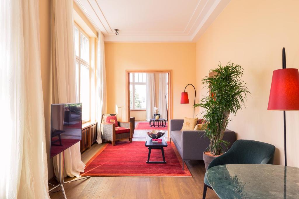 Boutique Hotels in Berlin Kreuzberg 15 Bright living room with large windows, gray sofa, green chair, TV, red area rug and lamps, potted plant, and glass coffee tableāreminiscent of the stylish interiors found in boutique hotels in Berlin Kreuzberg. Light walls and wood floors add warmth.