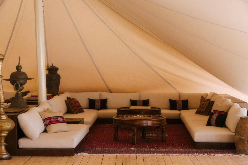 9 Best Hotels in Saudi Arabia: Unique Stays Across the Country 23 A cozy lounge area inside a canvas tent at one of the Best Hotels in Saudi Arabia features white cushioned sofas in a U-shape, colorful patterned pillows, a red rug, and wooden tables topped with decorative vases and lanterns.