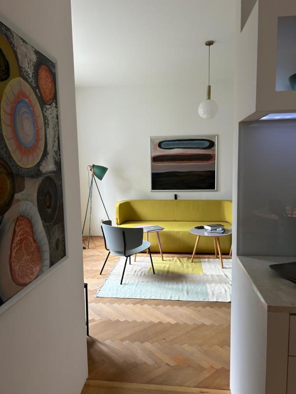 Where to Stay in Split: Hotel & Areas Guide 41 A modern living room, perfect for those searching where to stay in Split, with a yellow sofa, gray chair, round coffee table, floor lamp, abstract art, wooden herringbone flooring, and a white rug.