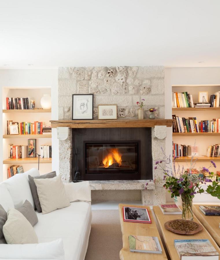 25 Weekend Trips from Madrid Max. 2h Away 63 A cozy living room with a stone fireplace, burning fire, wooden mantel with art and flowers—perfect for planning weekend trips from Madrid—built-in bookshelves on both sides, a white sofa with cushions, and a wooden coffee table with magazines and a flower vase.