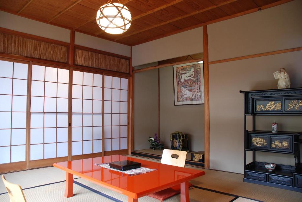 7 UNIQUE Ryokans in Gion Kyoto 17 A traditional Japanese tatami room, like those found in ryokans in Gion Kyoto, features a low red table with two chairs, shoji paper sliding doors, a decorative cabinet with ornaments, a hanging scroll, and a ceiling light.