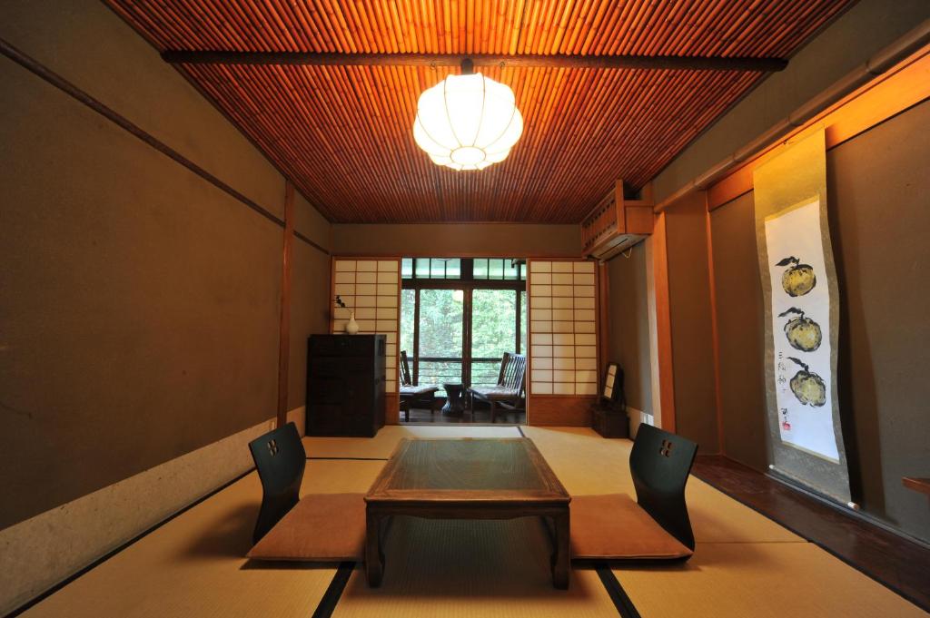 7 UNIQUE Ryokans in Gion Kyoto 20 Traditional Japanese tatami room with a low wooden table, two floor chairs, and shoji sliding doors—similar to the serene spaces found in ryokans in Gion Kyoto. Natural light enters from windows at the far end, highlighting elegant wall art.