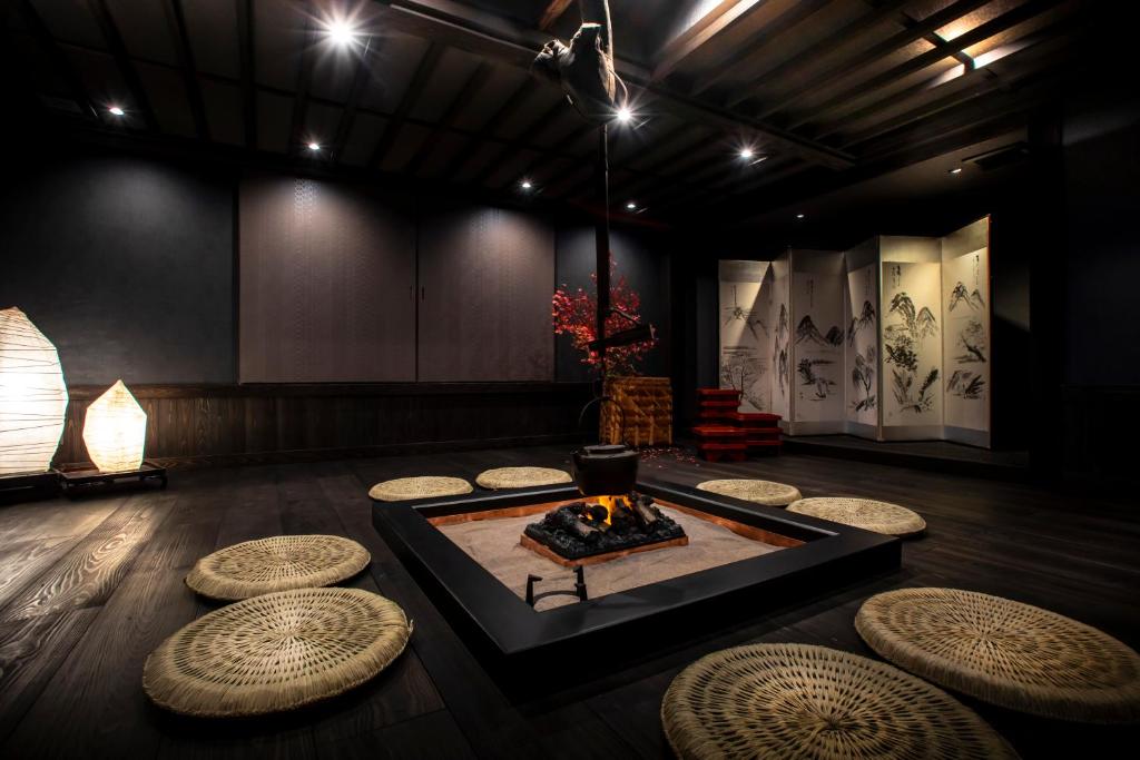 Looking for the Best Ryokan in Takayama? 16 A traditional Japanese room at the Best Ryokan in Takayama, featuring a sunken hearth encircled by woven straw cushions. A pot hangs over the fire, with dim lighting, dark wood floors, and a decorative folding screen in the background.