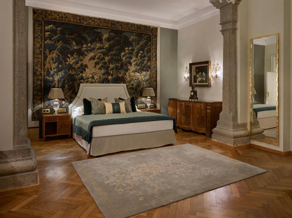 Unique Boutique Hotels in Salzburg 26 Elegant bedroom with a large bed, ornate headboard, and plush pillows—reminiscent of the charm found in boutique hotels in Salzburg. A tapestry hangs above the bed, flanked by lamps on wooden nightstands and a soft rug on a herringbone floor.