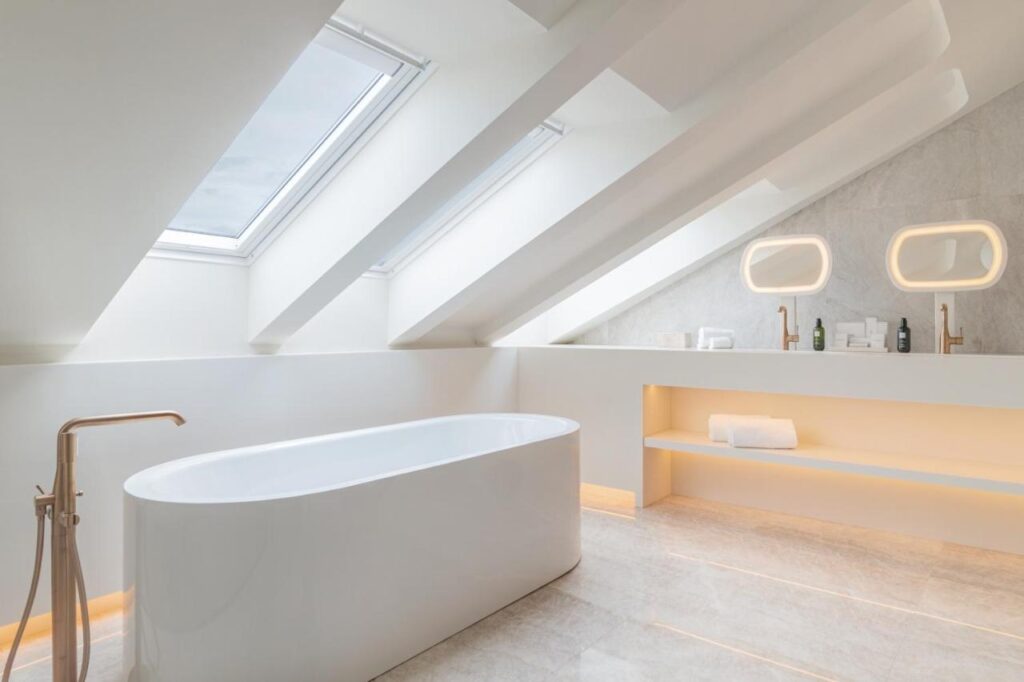 Where to Stay in Madrid: 14 Best Hotels 57 Minimalist attic bathroom with a freestanding white bathtub, skylights, slanted ceiling, modern fixtures, built-in shelves, and soft lighting—an inspiring design idea if you’re searching where to stay in Madrid first time with unique style.