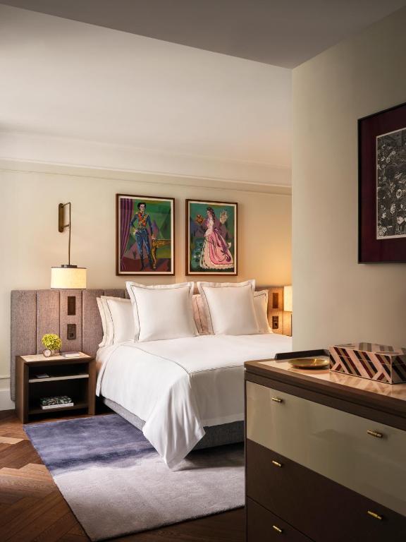 Authentic Boutique Hotels in Munich 29 A cozy, modern hotel room in the style of boutique hotels in Munich, featuring a neatly made double bed, two nightstands with lamps, colorful art above the bed, a small rug, and a chest of drawers in the foreground.