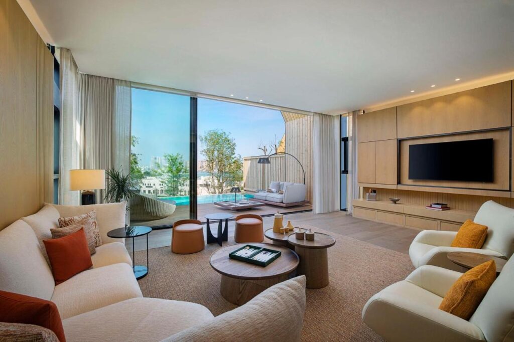Where to Stay in Doha, Qatar: Transit, City & Beach Hotels 10 Modern living room with neutral tones, featuring white and beige sofas, round wooden coffee tables, and a large flat-screen TV—perfect inspiration when deciding where to stay in Doha with stylish comfort and stunning patio views.