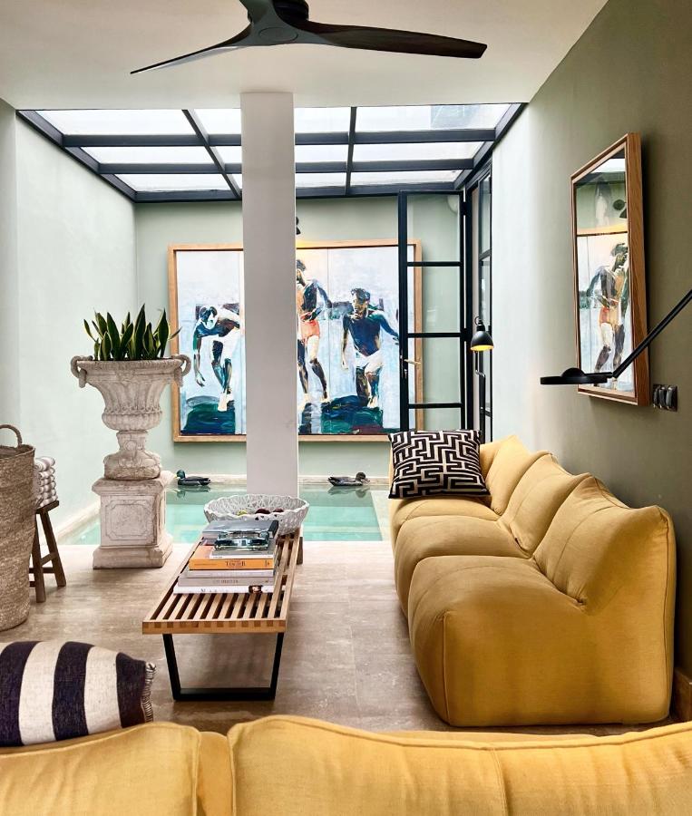 9 UNIQUE Riads in Tangier 23 Bright modern living room with yellow sofas, a glass coffee table, indoor plants, and a pool. Large abstract artwork and a wall mirror decorate the mint-green walls, evoking the elegance of riads in Tangier.