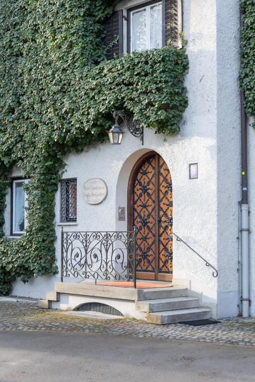 Authentic Boutique Hotels in Munich 8 A building facade covered in green ivy, like those seen at boutique hotels in Munich, features a window with a white frame and a balcony with ornate black railings next to a wooden arched door with decorative ironwork. Steps lead up to the entrance.