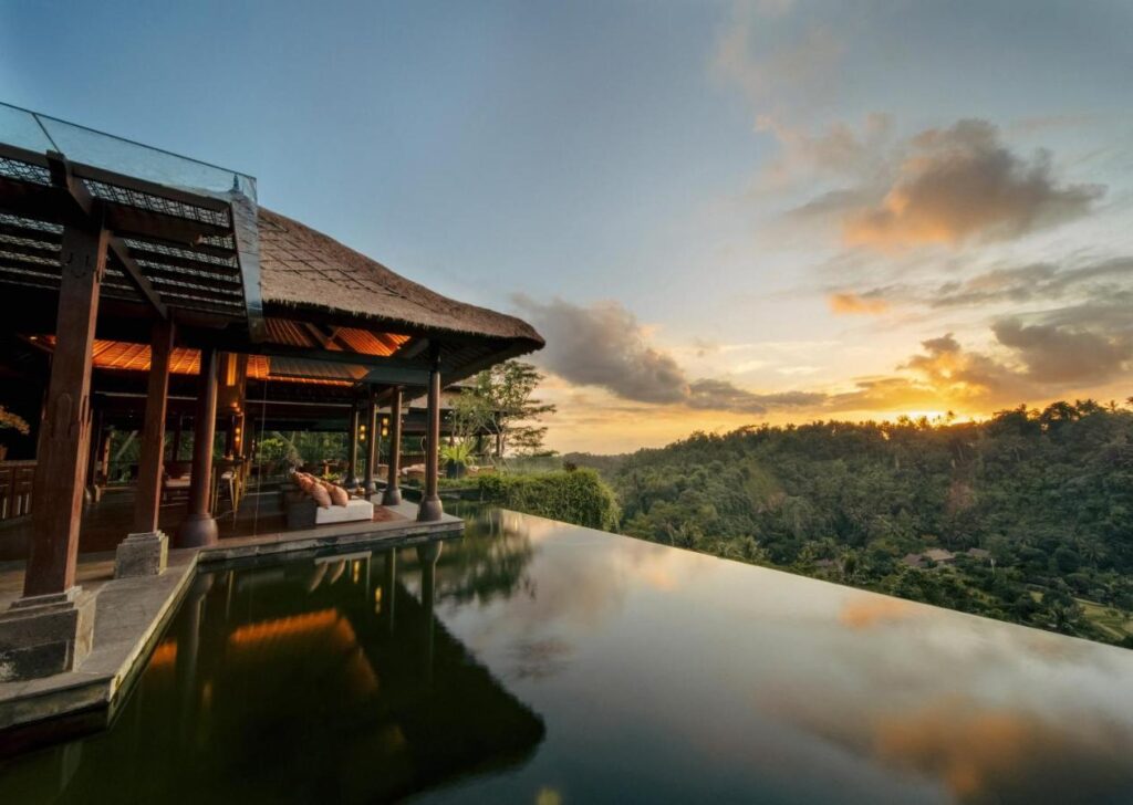 13 Most UNIQUE Places to Stay in Ubud 49 A luxurious villa with an infinity pool overlooks a lush green valley at sunset—one of the most unique places to stay in Ubud, where warm orange skies and serene reflections create an unforgettable escape.