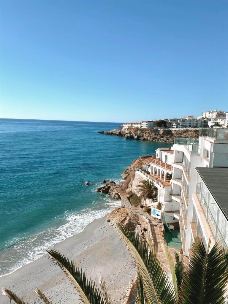 Adults-Only Hotels in Costa del Sol 3 A sunny coastal scene with clear blue skies, turquoise sea, white sandy beach, palm trees, and white seaside buildings—perfect for those seeking the exclusivity of adult only hotels in Costa del Sol overlooking the water.