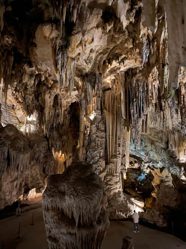 Adults-Only Hotels in Costa del Sol 2 A large cave interior filled with dramatic limestone stalactites and stalagmites, illuminated by soft artificial lighting. A person stands near the formations, reminiscent of adventures found near adult only hotels in Costa del Sol.