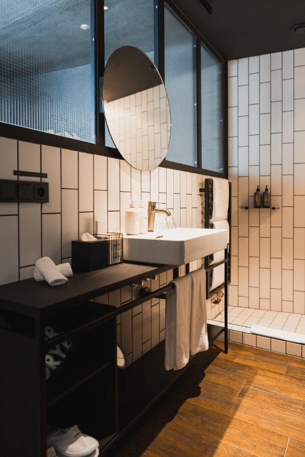Where to Stay in Reykjavík: Top Guide 13 Modern bathroom with white rectangular tiles, a round mirror above a white sink, neatly arranged toiletries, black fixtures, and wooden floor—perfect inspiration for those seeking stylish amenities when deciding where to stay in Reykjavik.
