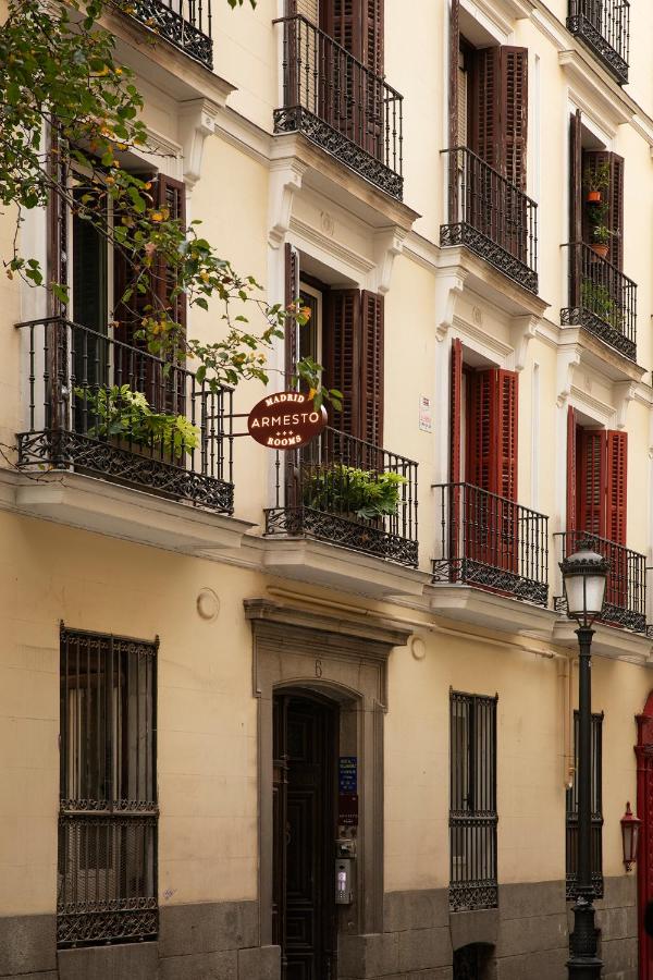 Where to Stay in Madrid: 14 Best Hotels 7 A beige building with multiple balconies and brown shutters, some open, displays a round “Madrid Armesto Rooms” sign above the entrance—a charming option for where to stay in Madrid first time visitors. Green plants decorate balconies, with a lamppost nearby.