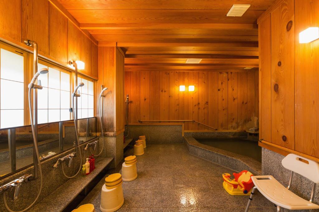 Looking for the Best Ryokan in Takayama? 12 A traditional Japanese bathhouse at the Best Ryokan in Takayama, featuring wooden walls and ceiling, shower stations with stools and mirrors on the left, yellow buckets on the floor, and a large soaking tub at the back. The warm lighting is inviting.
