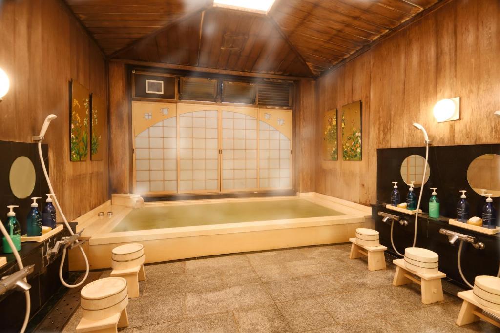 7 UNIQUE Ryokans in Gion Kyoto 14 A traditional Japanese onsen room at ryokans in Gion Kyoto, featuring wooden walls and ceiling, a rectangular hot spring bath, low stools, hand showers, and bottles of soap and shampoo. Soft lighting creates a warm, relaxing atmosphere.