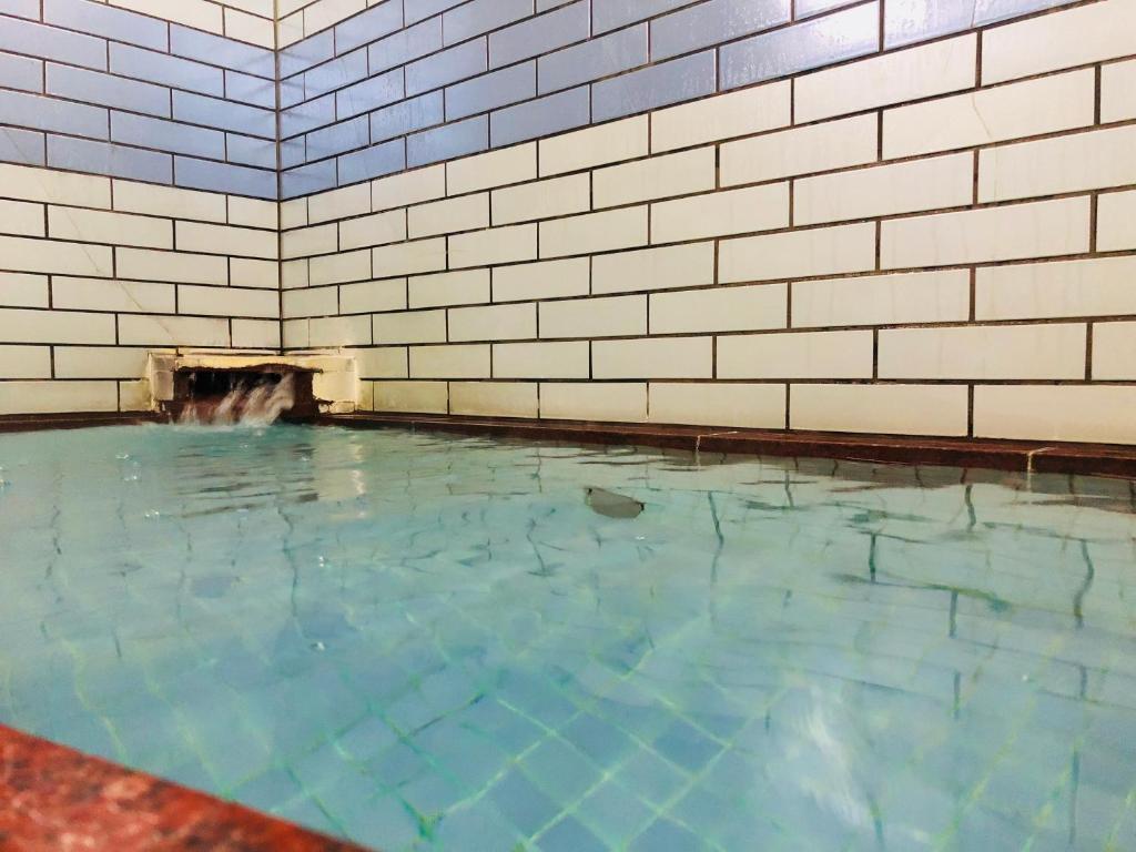 Looking for the Best Ryokan in Takayama? 20 Small indoor pool with clear water, surrounded by white and light blue tiled walls. Water flows gently from a spout set into the wall, creating slight ripples—an inviting retreat at the Best Ryokan in Takayama.