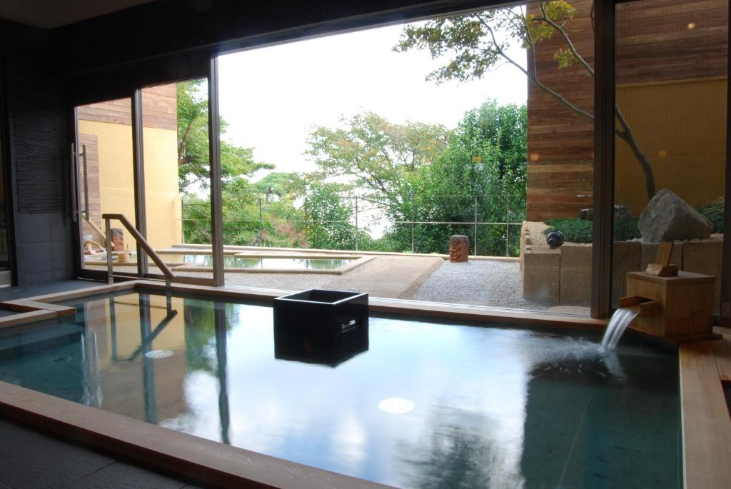 8 BEST Ryokans in Osaka 30 Indoor hot spring bath with clear water and wooden edges, overlooking a peaceful outdoor area with greenery and another hot spring pool through large glass windows—typical of traditional ryokans in Osaka.