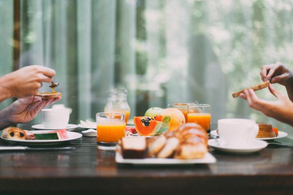 4 Best Hotels in Ribera del Duero, Spain 14 Two people sit at a table enjoying breakfast with pastries, toast, fruit, orange juice, and coffee—a perfect start before exploring weekend trips from Madrid. The bright scene is filled with natural light and greenery in the blurred background.