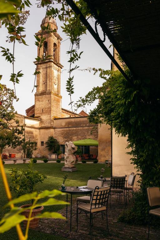 7 Best Agriturismos in Tuscany 10 A serene courtyard with tables and chairs, greenery, and a large stone statue; in the background, a historic stone church tower rises against the sky—evoking the timeless charm of the best agriturismos in Tuscany.