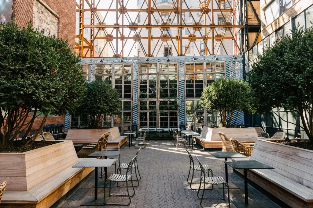 11 Unique Hotels in Georgia You Can't Miss! 14 Outdoor courtyard with modern seating, square tables, potted trees, and wooden benches. Glass walls, exposed yellow metal beams, and arched windows create a stylish backdropāperfect for guests seeking unique hotels in Georgia.
