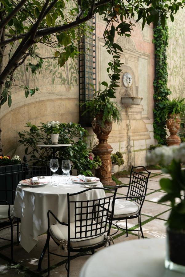 Where to Stay in Madrid: 14 Best Hotels 49 A round table set for two with wine glasses and plates sits in a lush, elegant courtyard beside a decorative stone fountain—capturing the serene outdoor dining atmosphere perfect for those exploring where to stay in Madrid first time.