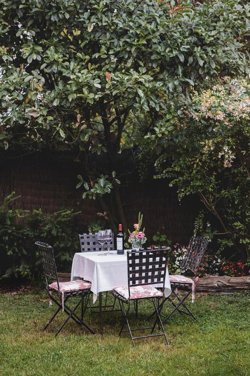 8 Unique Boutique Hotels in Bilbao Spain 27 A small outdoor table with a white tablecloth, four black chairs, a bottle of wine, and a vase of flowers is set on green grass in a lush garden—reminiscent of the charming ambiance at boutique hotels in Bilbao.