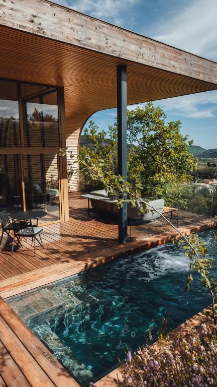 11 Unique Places to Stay in Provence 23 A modern wooden house with large glass windows features a patio, outdoor seating, and a small private pool—one of the unique places to stay in Provence, surrounded by greenery and scenic hillside views under a blue sky.