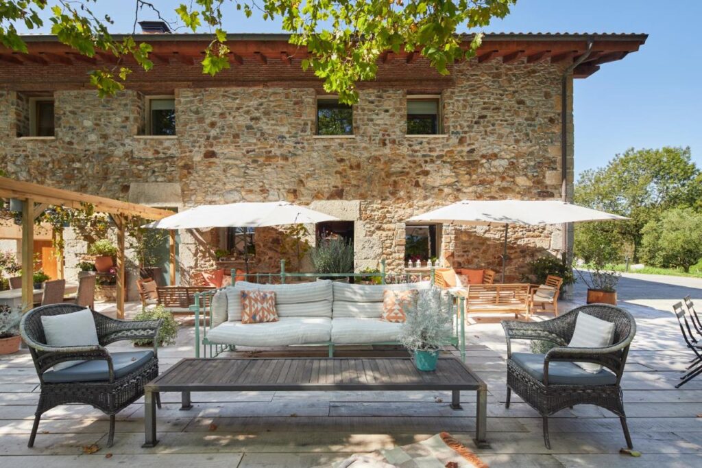 Best Boutique Hotels in San Sebastian 4 A rustic stone house with a spacious patio featuring wicker furniture, a cushioned sofa, and potted plants. Surrounded by greenery, it offers the charm and comfort often found in boutique hotels in San Sebastian.