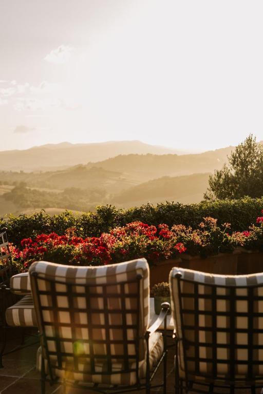7 Best Agriturismos in Tuscany 17 Two cushioned patio chairs face a low wall lined with blooming red and pink flowers, overlooking the scenic rolling hills you’ll find at agriturismos in Tuscany, all glowing beneath a bright, golden sunset sky.