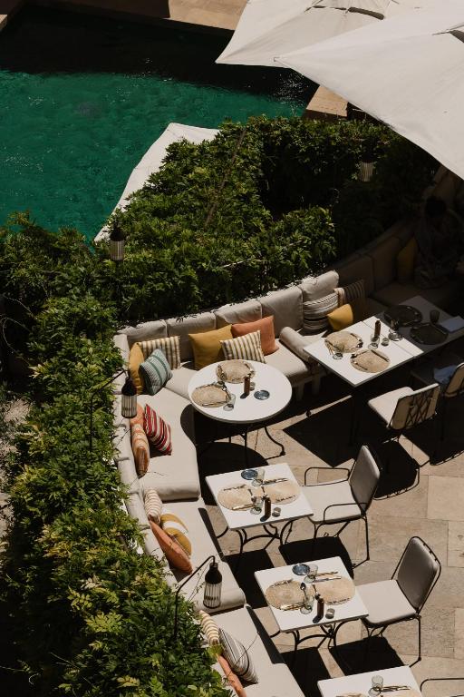 11 Unique Places to Stay in Provence 33 Aerial view of an outdoor dining area with cushioned seating, colorful pillows, and set tables, surrounded by green bushes next to a turquoise swimming pool—one of the unique places to stay in Provence under partial shade.
