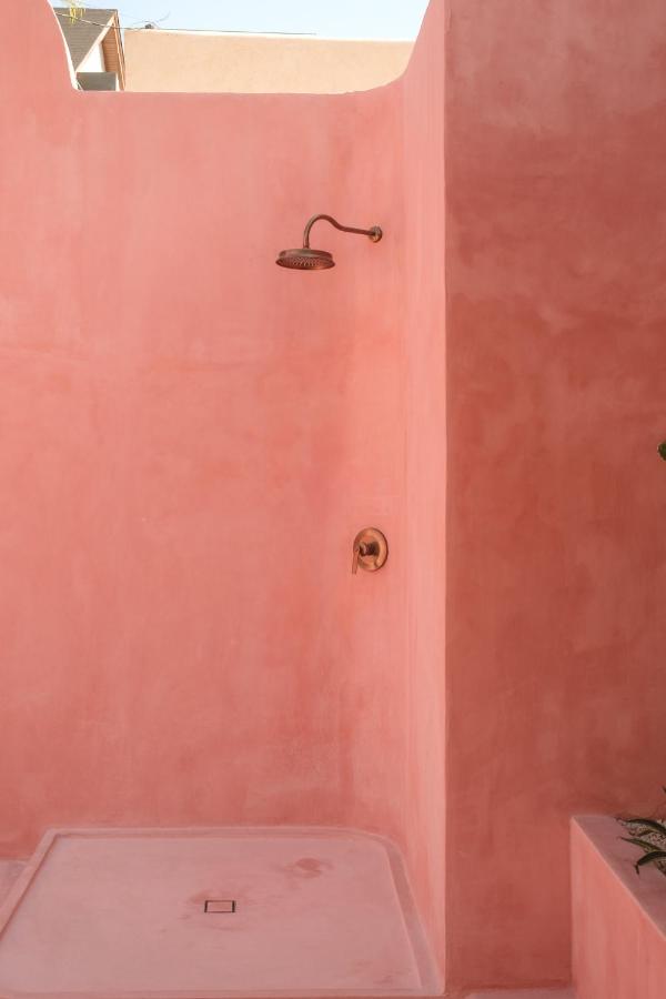 Outdoor shower area with smooth, pastel pink walls and bronze showerhead, typical of the best family villas in Bali. Sunlight casts soft shadows, creating a warm and minimalistic atmosphere with simple fixtures.