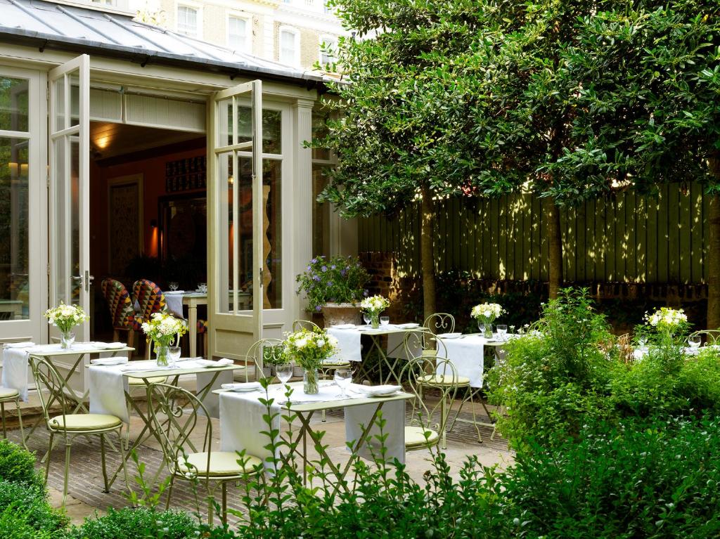 15 Best Boutique Hotels in London, UK 55 An outdoor garden cafe with elegant metal tables and chairs, each table set with white tablecloths and flower arrangements, surrounded by lush greenery—an ambiance often found at boutique hotels in London, next to open glass doors leading inside.