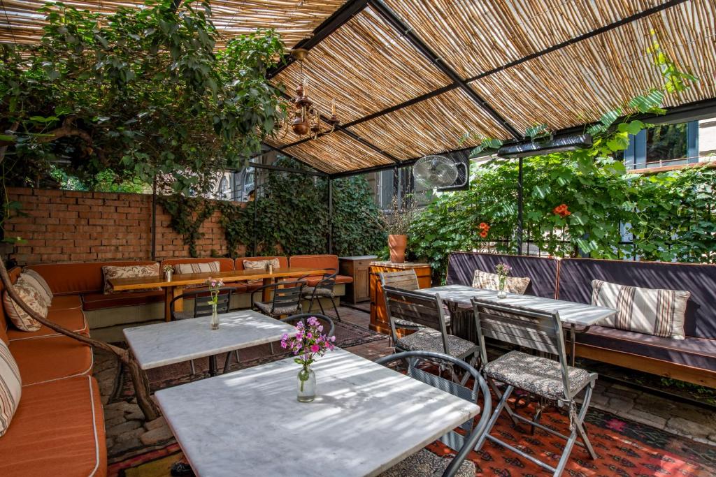 11 Unique Hotels in Georgia You Can't Miss! 27 Cozy outdoor seating area with cushioned benches, metal chairs, and marble tables, surrounded by lush greenery and brick walls under a bamboo-covered pergolaāan inviting spot often found at unique hotels in Georgia. Small vases with flowers decorate the tables.