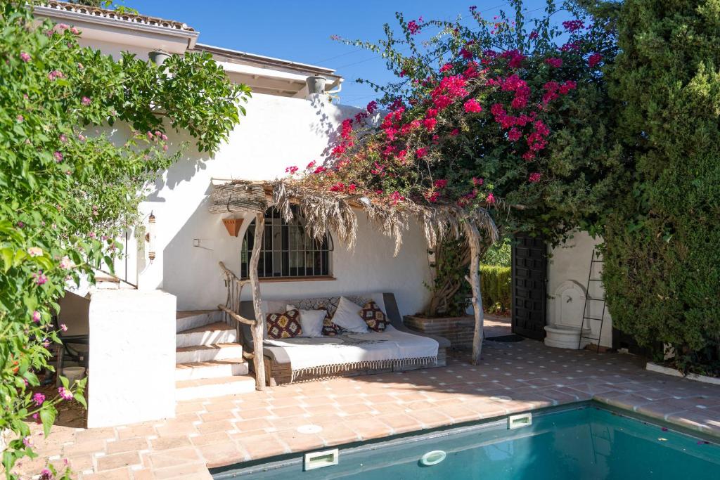 Adults-Only Hotels in Costa del Sol 30 A cozy outdoor seating area with cushions sits under a thatched pergola draped in bougainvillea, beside a turquoise pool—evoking the tranquil charm of adult only hotels in Costa del Sol. White walls and lush greenery enclose this sunlit Mediterranean-style patio.
