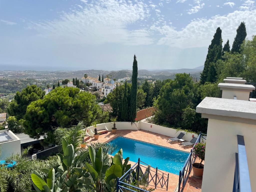 Adults-Only Hotels in Costa del Sol 21 A swimming pool with blue water, found at one of the adult only hotels in Costa del Sol, is surrounded by a tiled patio, lush greenery, and tall trees overlooking distant hills and white buildings under a partly cloudy sky.