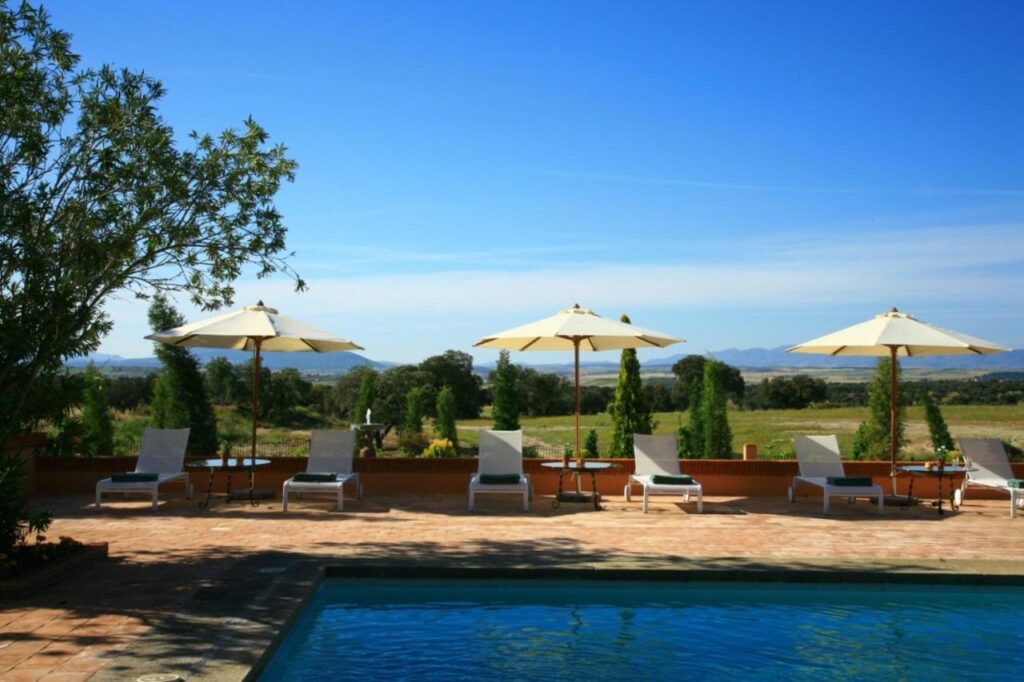 25 Weekend Trips from Madrid Max. 2h Away 9 Relax poolside with lounge chairs and white umbrellas, surrounded by green fields and distant hills—an ideal spot for weekend trips from Madrid under a clear blue sky.